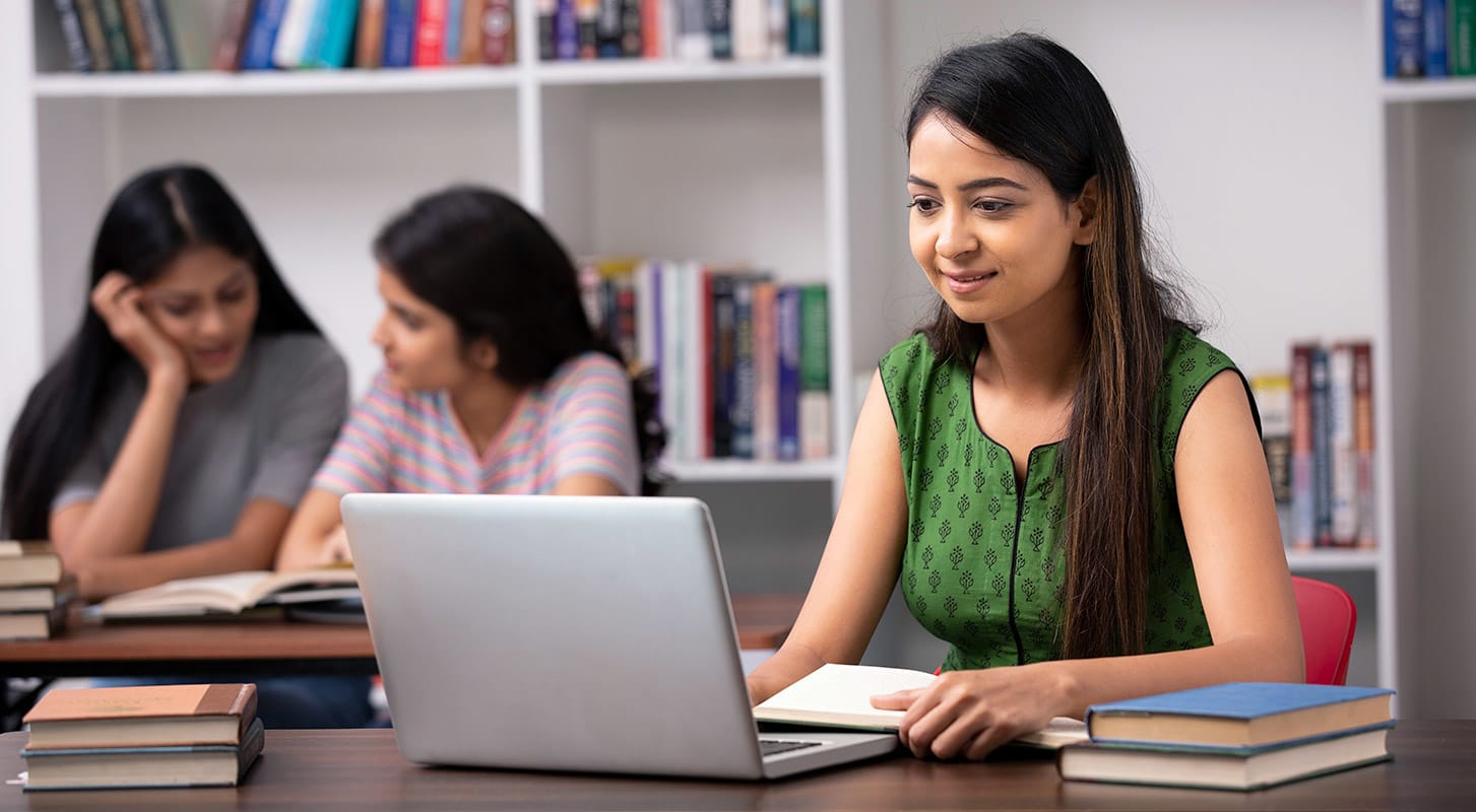 A woman seated at a desk with a laptop, immersed in work among shelves of books in a library.